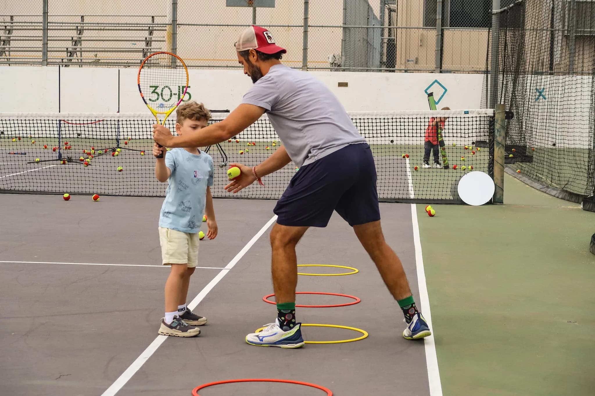 Tennis coach guiding a young player during a beginner tennis lesson on an outdoor court in Glendale.