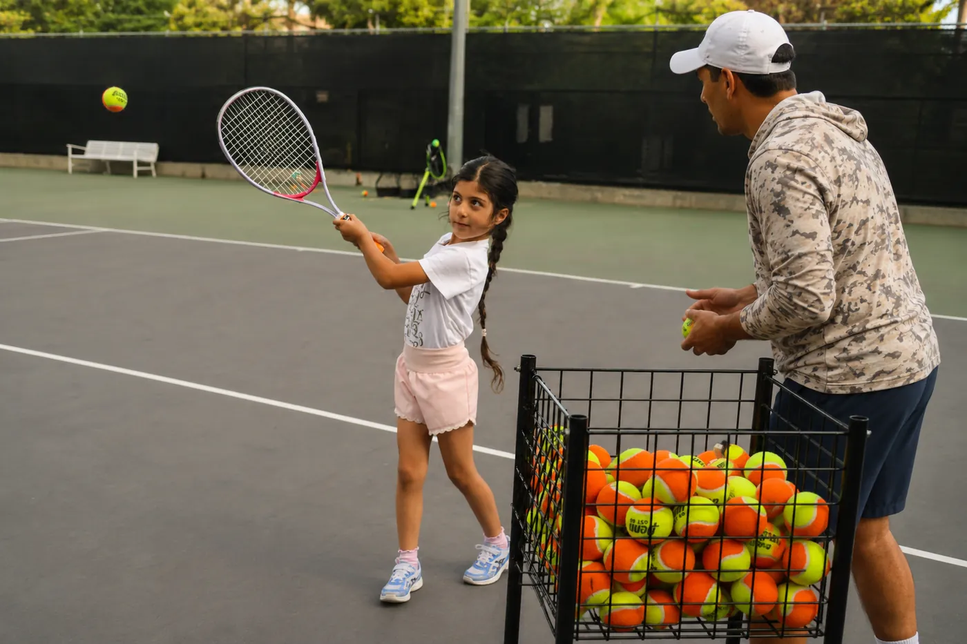A young player practicing a forehand with a coach on an outdoor tennis court