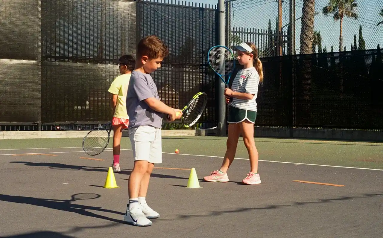Junior players practicing tennis with rackets and training cones